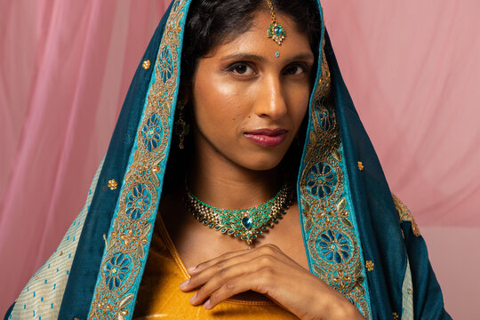 Indian woman posing wearing teal dupatta and green-gold choker and tikka, touching neck in studio