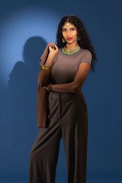 African American woman standing and posing in studio holding brown blazer with green-gold jewelry