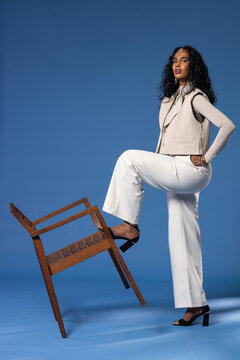 Indian woman posing on blue set, wearing vest, jewelry, resting on chair, copy space