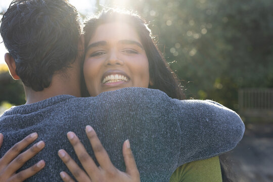 Indian couple hugging, woman smiling into camera outdoors on path with green top, gray sweater