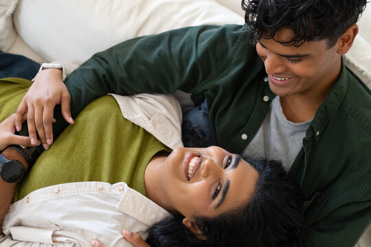 Diverse couple reclining on light sofa at home, wearing green and beige tops with wristwatches