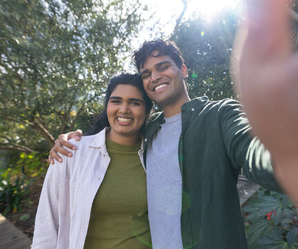 Diverse couple in casual shirts smiling and posing while taking selfie in garden phone lens flare