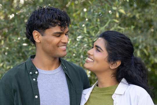Indian couple standing chest-up in garden, wearing dark green shirt and light overshirt, smiling