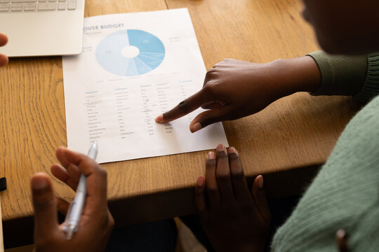 African team pointing at budget sheet with pie-chart on table, woman wearing green sweater with pen
