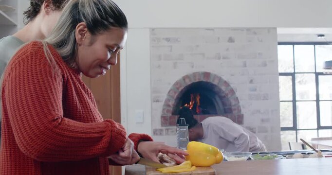 Diverse friends prepping kitchen island, woman chopping pepper, man tending oven flames, copy space
