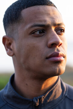 African American man looking right, wearing dark zip-up jacket with visible zipper pull outdoors