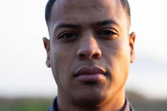 African American man in mid-20s gazing at camera outdoors in golden hour wearing dark jacket
