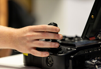 Hand adjusting control joystick on professional electronic equipment with buttons, dials, cables, and monitor in an indoor workspace © HelgaQ