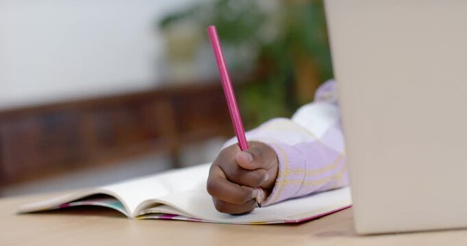 Child's hand is adjusting grip and making marks in notebook on desk as pencil nears page
