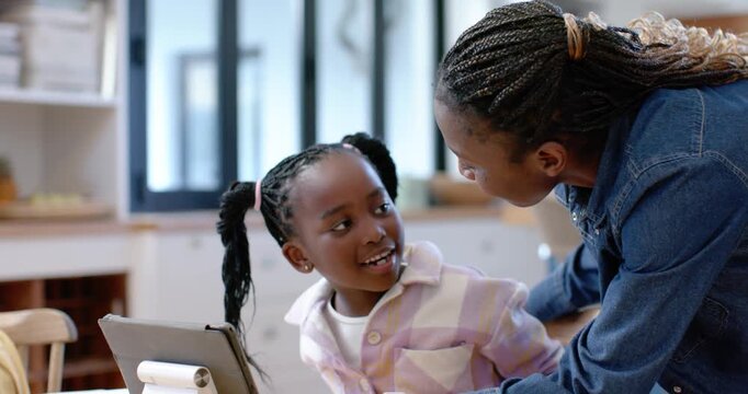 African American woman leaning guiding child, child tapping tablet on white stand at home for study