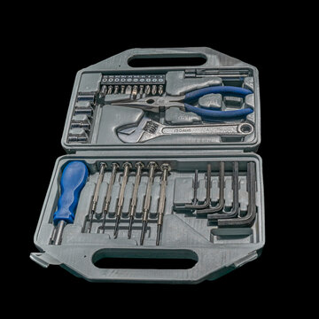 An open gray plastic carrying case displaying a comprehensive hand tool kit including needle-nose pliers, an adjustable wrench, precision screwdrivers, Allen keys, and driver bits.