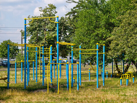 Yellow and blue outdoor workout station with gymnastic rings pull up bars parallel bars and training equipment in a residential neighborhood for strength exercise and recreation