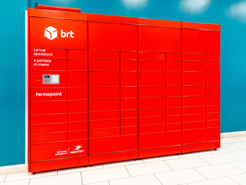 Italy - October 9, 2026: Red automated parcel locker station by BRT Fermopoint and Geopost, located indoors on  white tiled floor against  bright blue wall. Secure self-service smart locker system 