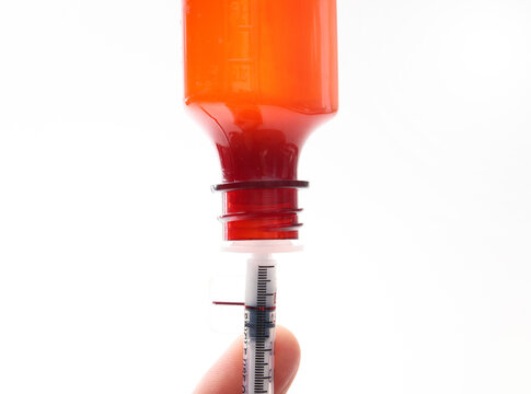 Oral steroid medication bottle with dosing syringe. Liquid anti-inflammatory for pets or children, dispensed by owner or parent. Dosage line visible. Selective focus.