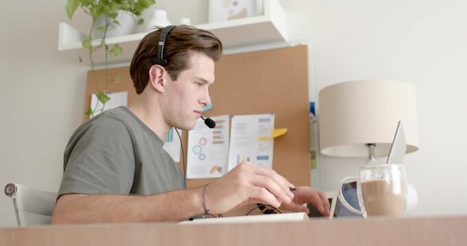 Man receiving phone notification writing notebook and typing on laptop smiling with headset at desk