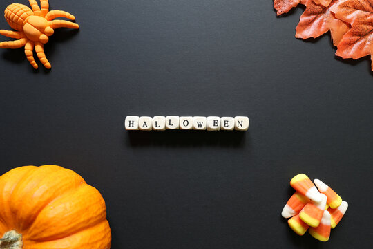Halloween spelled with letter tiles on black with pumpkin, candy corn, toy spider and autumn leaves, creating a festive seasonal background.