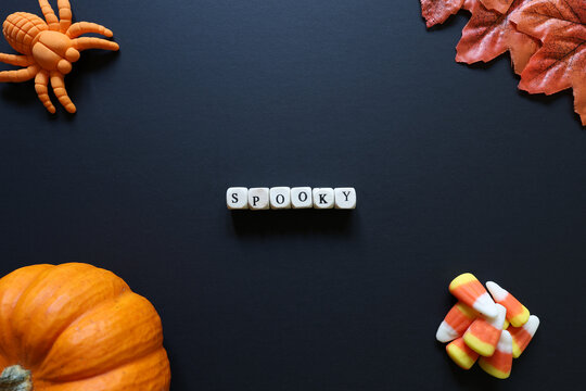 Spooky spelled with letter tiles on black background with pumpkin, candy corn, toy spider and autumn leaves for a Halloween concept.