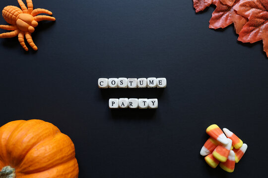 Costume Party spelled with letter tiles on black background with pumpkin, candy corn, toy spider and autumn leaves for a festive Halloween concept.