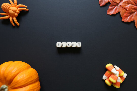 Scary spelled with letter tiles on black background with pumpkin, candy corn, toy spider and autumn leaves for a Halloween concept.