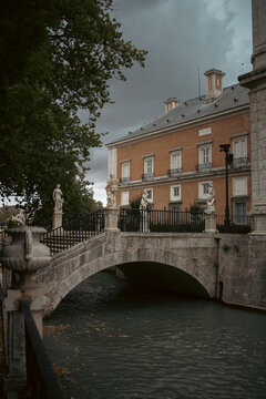 Stone bridge with statues leading to a historic brick palace 