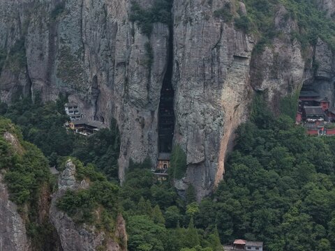 Aerial view of towering karst mountains in Lingfeng, Yandangshan, China, with a traditional temple nestled below. Dramatic limestone peaks and lush vegetation dominate the landscape.