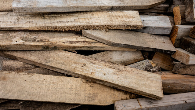 Pile of weathered, rough-cut wooden planks and scrap lumber stacked irregularly. Abstract Construction Background