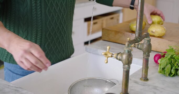 Brass-tap urging sweater man at kitchen sink rubbing spuds, rinsing radishes into colander for meal