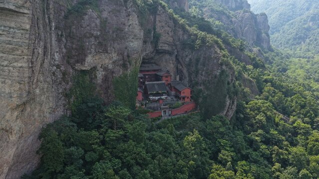 Aerial view of towering karst mountains in Lingfeng, Yandangshan, China, with a traditional temple nestled below. Dramatic limestone peaks and lush vegetation dominate the landscape.