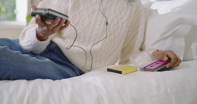 Adult woman picking pink cassette opening deck plugging wired earphones listening on bed in sweater