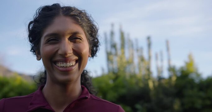 Camera approaching African American woman wearing maroon top turning, smiling, laughing in garden