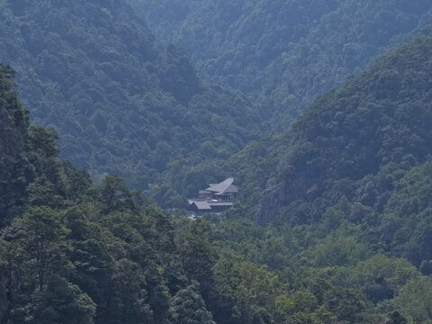 Aerial view of towering karst mountains in Lingfeng, Yandangshan, China, with a traditional temple nestled below. Dramatic limestone peaks and lush vegetation dominate the landscape.