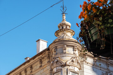 Ornate historic building corner turret roof detail with decorative finial and hanging orange flower basket in old town Kosice city center Slovakia under clear blue sky architectural heritage scene © Soloviova Liudmyla