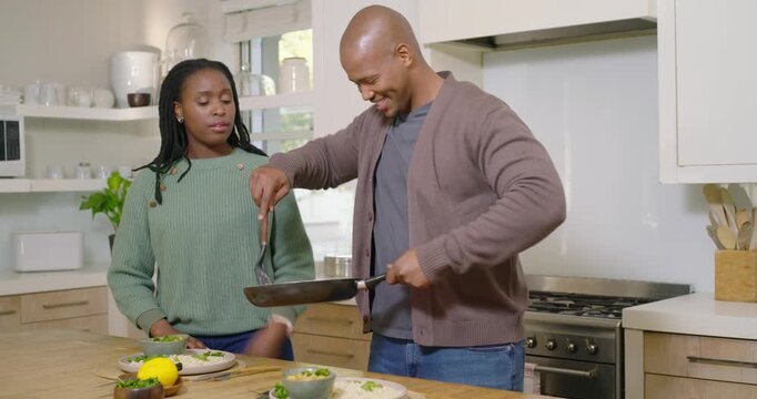 African American couple plating at kitchen island, man bringing pan and scooping food with spatula