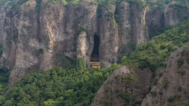 Aerial view of towering karst mountains in Lingfeng, Yandangshan, China, with a traditional temple nestled below. Dramatic limestone peaks and lush vegetation dominate the landscape.