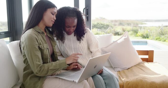 African American women noticing open silver laptop, collaborating, typing and pointing on sofa