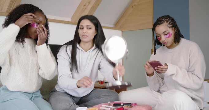 Laying cloth, Three African American women on bed, applying patches and testing makeup in mirror
