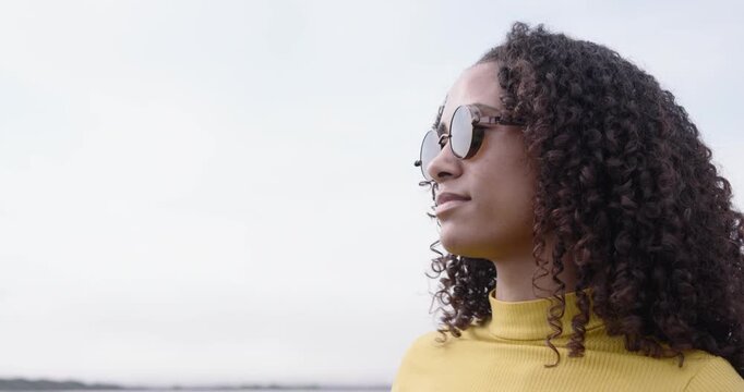 African American woman in yellow top seeing waterfront smiling adjusting tortoise shades