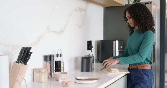 African American woman putting bread in toaster, cutting avocado on board for breakfast, copy space