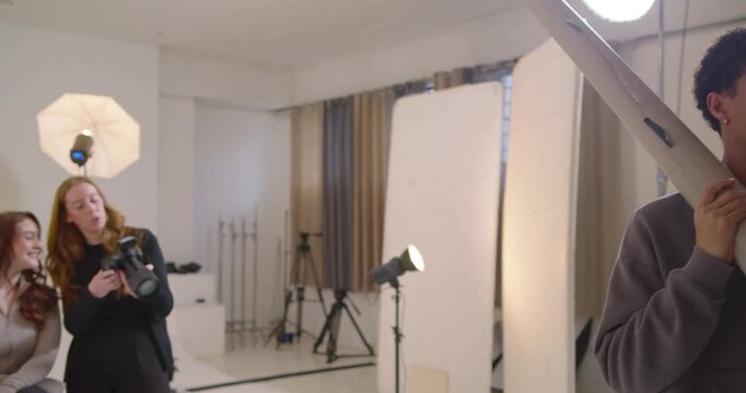 Diverse crew prepping shoot in studio, assistant entering left holding roll, woman checking camera