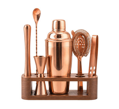 Complete set of shiny copper bar tools with a shaker and jigger stands elegantly in a wooden holder on a white background