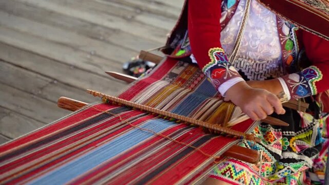 Slow-motion close-up of Andean hands weaving while wearing colorful traditional Peruvian clothing