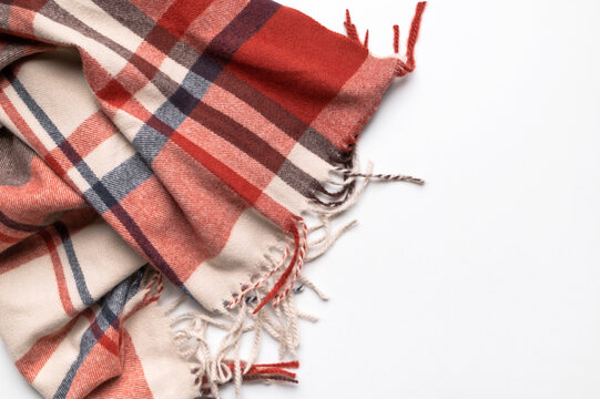 Autumn scarf in burgundy plaid lies folded on light gray background, with visible fringe and woven texture. Fashion marketing can present seasonal apparel, classic pattern, warmth and casual styling.