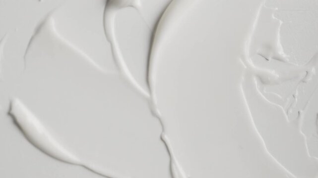 White cosmetic cream smearing on a surface with a spatula creating a smooth texture for beauty and skincare advertising