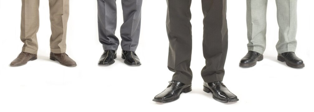 Four businessmen standing in a row with one standing further forward, detail of legs