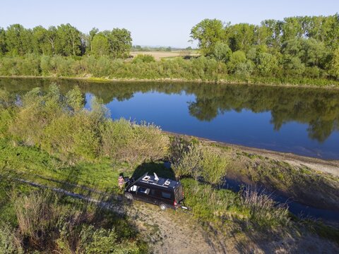 A car is parked next to a quiet river under trees, which gives a relaxed camping atmosphere, aerial view, motorhome, camper, Somes river near Satu Mare, Somesch, Satu Mare, Romania