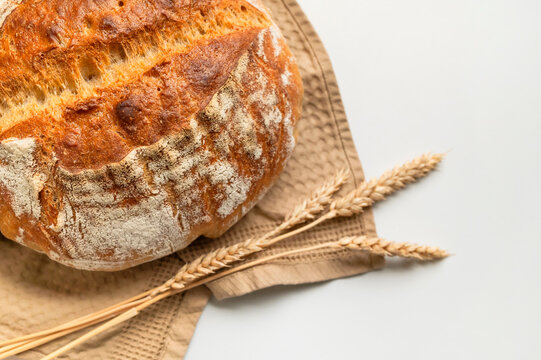 Fresh rustic bread sits on kitchen towel with wheat ears, highlighting handmade baking and grain heritage. Warm food styling suits bakery marketing, recipe content, culinary lessons, packaging.