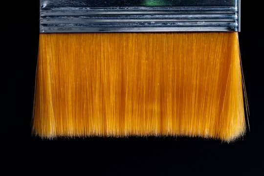 Orange paint brush bristle closeup. Macro view of yellow synthetic paintbrush hairs with metal ferrule. Abstract art texture backdrop for painting, renovation, creative hobby and hardware store