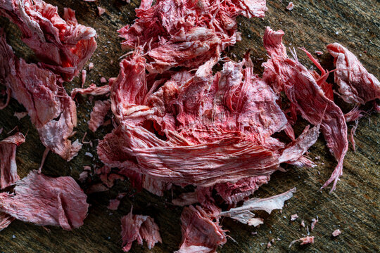 Dried red ginger fibers on wooden board closeup. Top view of candied red ginger slices on wood background. Dehydrated sweet ginger root pieces for healthy snack concept, dessert recipe and marketing