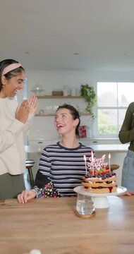 Vertical video: Diverse friends placing HAPPY sash, clapping at kitchen with cake for birthday star