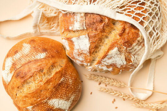 Round sourdough bread sits inside cotton mesh bag on beige background. Reusable textile packaging highlights sustainable shopping, bakery products, natural food, and low waste lifestyle.